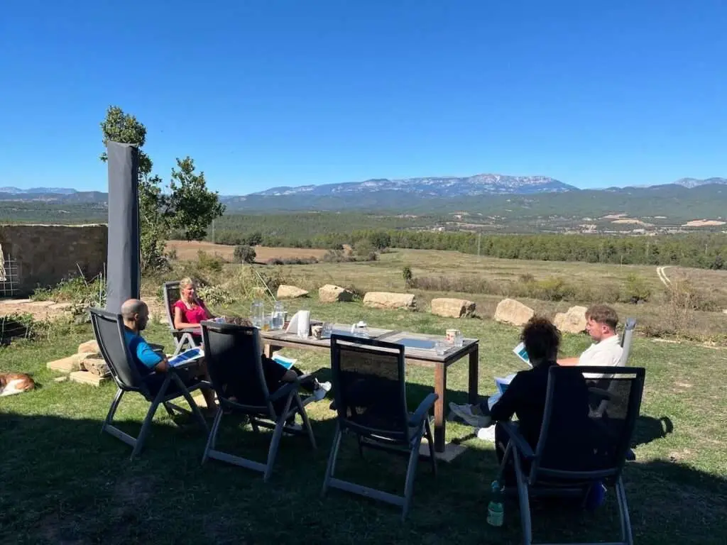 Astrid geeft in de tuin uitleg aan groep deelnemers met blauwe lucht op de achtergrond.