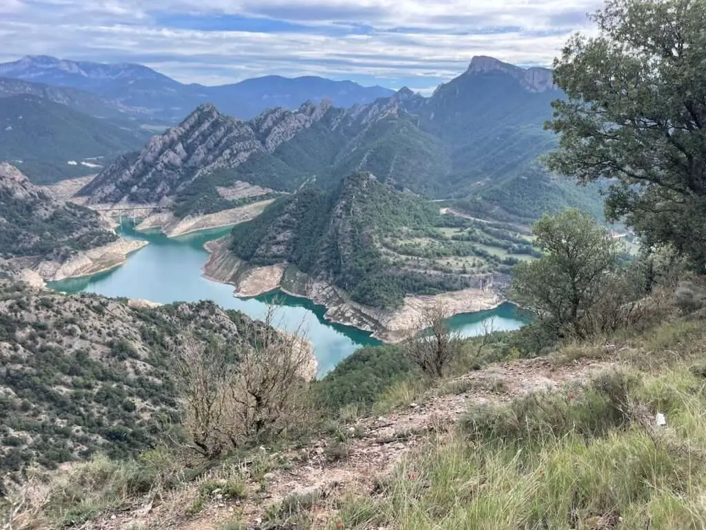 Helder bergmeer omringd door groene heuvels onder een blauwe lucht.