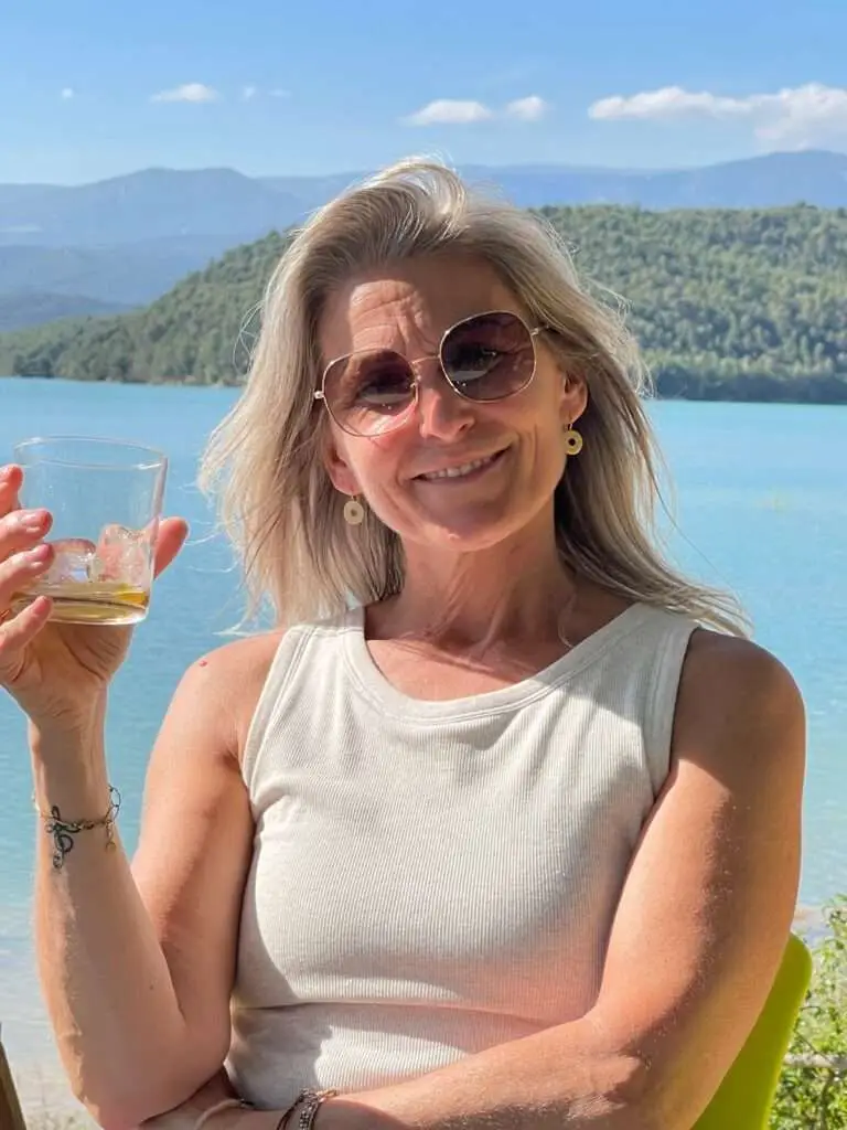 Deelnemer met drankje in de hand met op de achtergrond een meer en bergen.