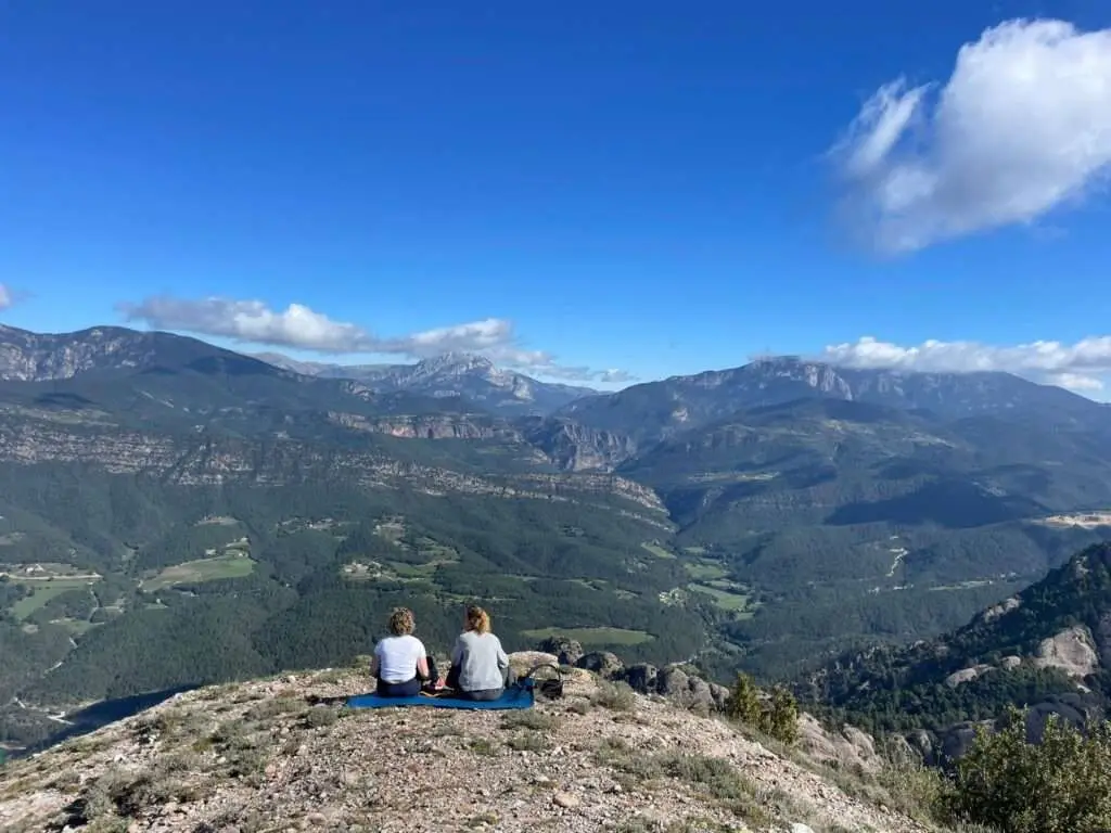 Deelnemers die op een rotspunt zitten en uitkijken op bergen en blauwe luchten.