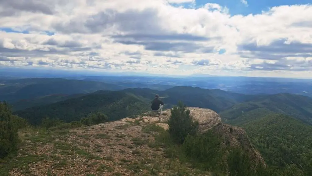 Man zittend op rots met wijd uitzicht over het landschap.